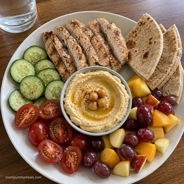Chicken hummus snack plate with cucumber tomatoes fruit and whole grain pita