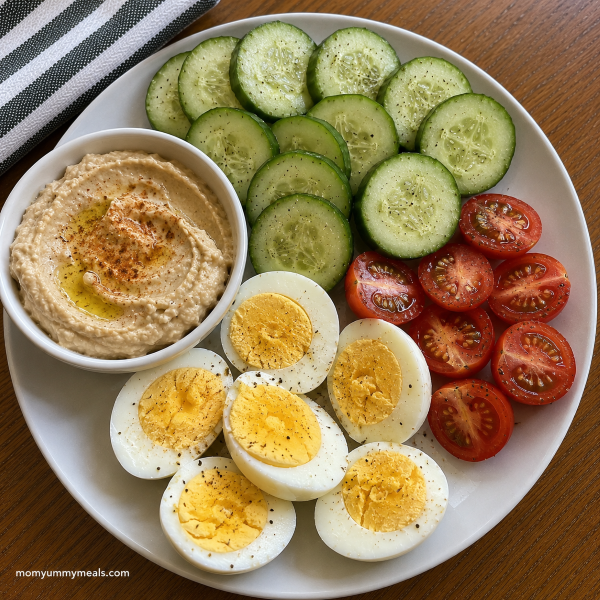 Hard boiled egg snack plate with cucumber tomatoes and hummus