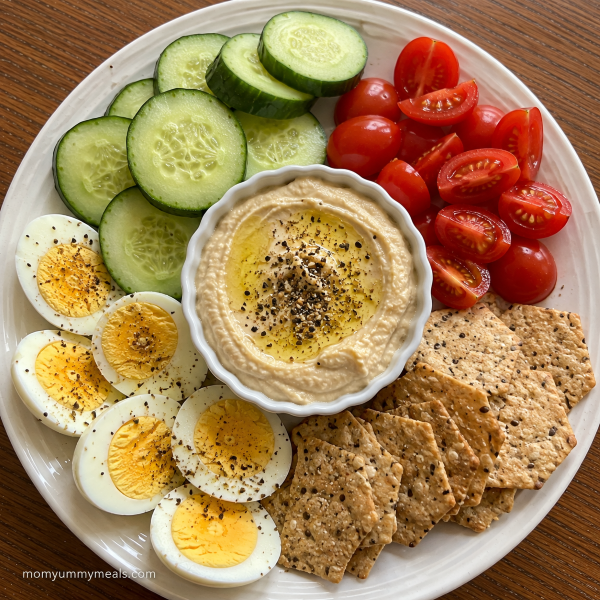 Hard boiled egg snack plate with hummus cucumber tomatoes and crackers