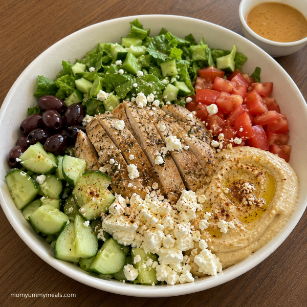Mediterranean chicken bowl with hummus cucumber tomatoes greens and feta