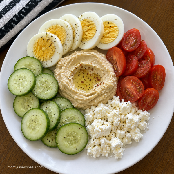 Mediterranean snack plate with hard boiled egg hummus cucumber tomatoes and feta