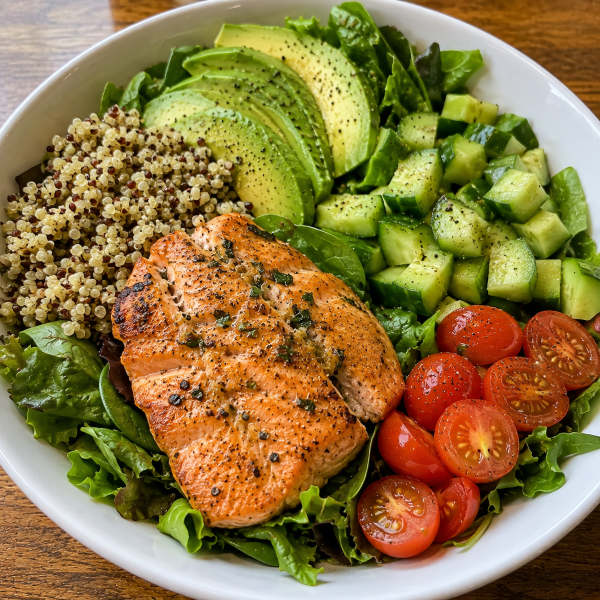Salmon avocado bowl with cucumber tomatoes greens and quinoa