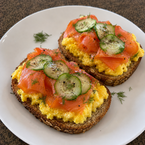 Whole grain toast topped with scrambled eggs smoked salmon and cucumber