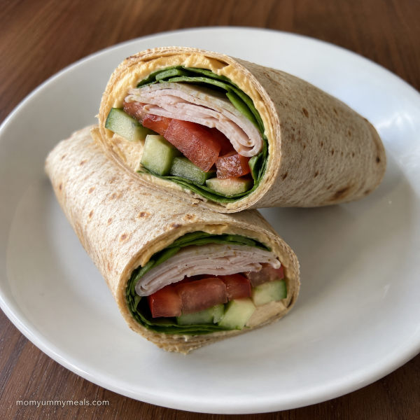 Whole grain turkey hummus wrap with spinach cucumber and tomatoes